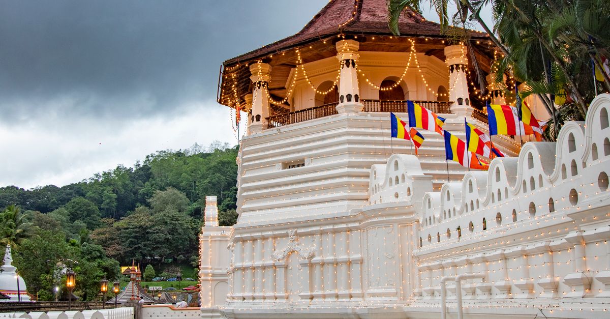 Beautiful view of a sacred temple reflecting in the river, surrounded by lush greenery, under a moody sky in Sri Lanka.